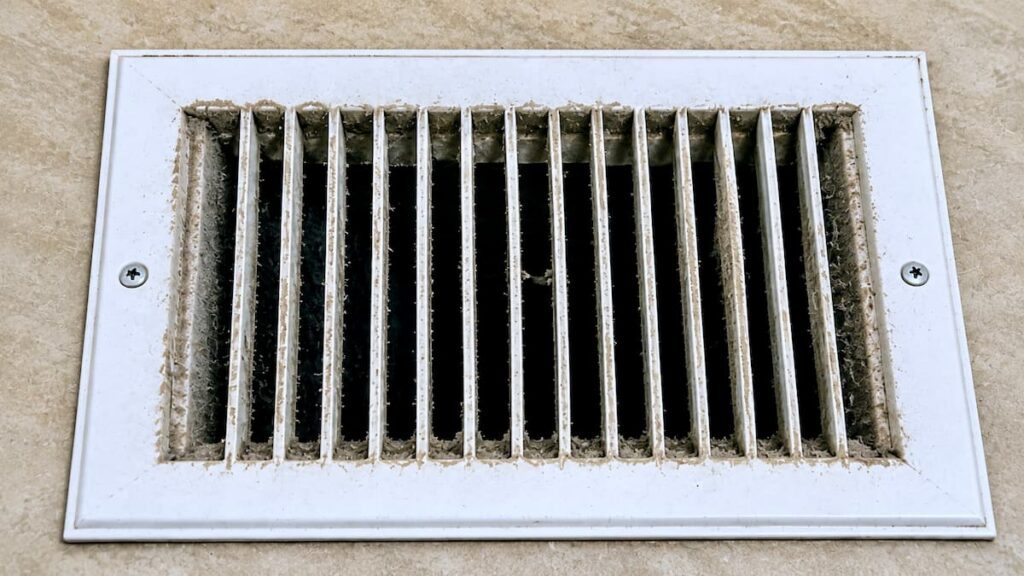 A residential ceiling supply register with visible dust accumulation around the louvers.